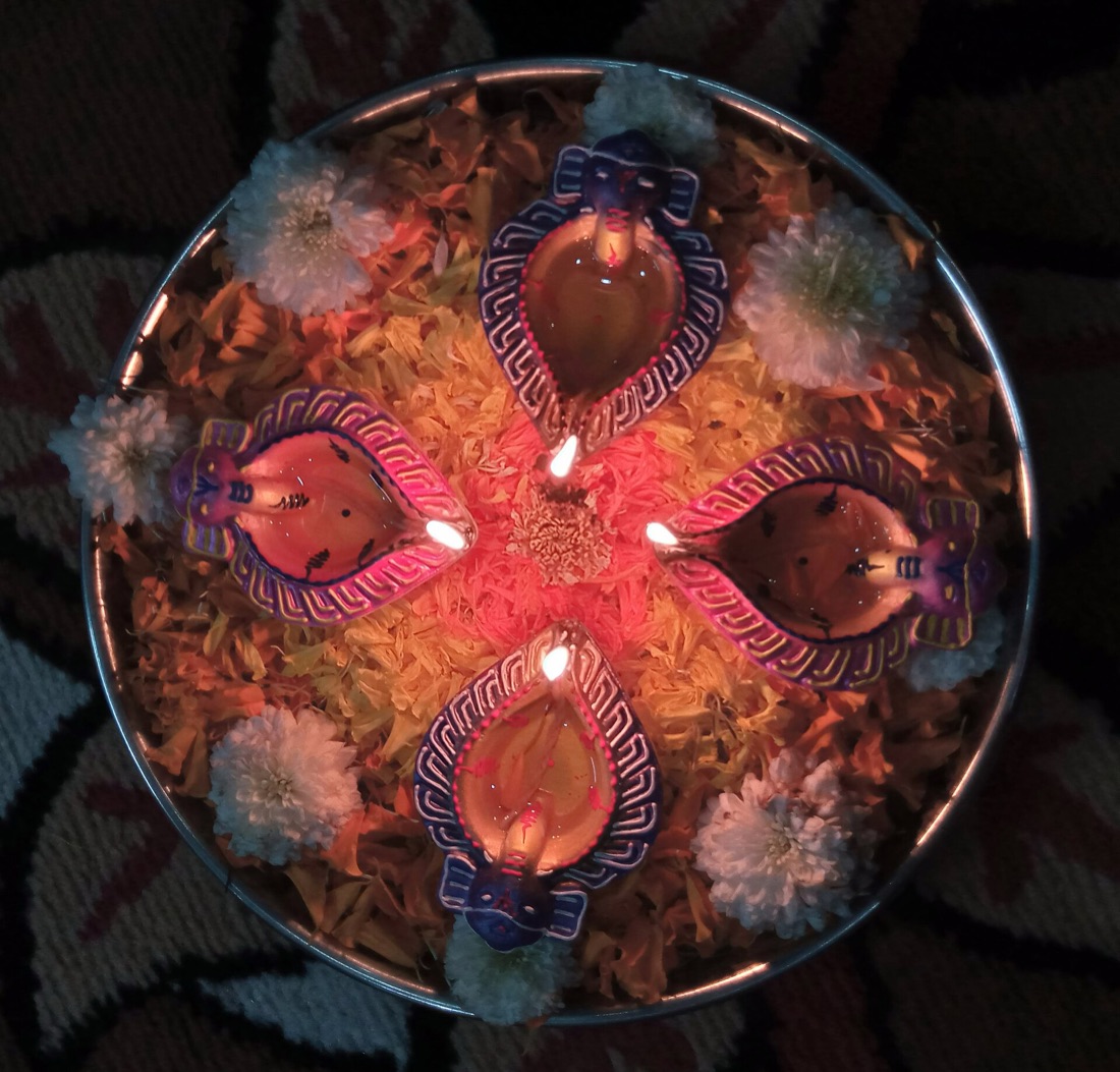 Four hand-painted clay diyas lit on a plate of marigold and chrysanthemum petals
